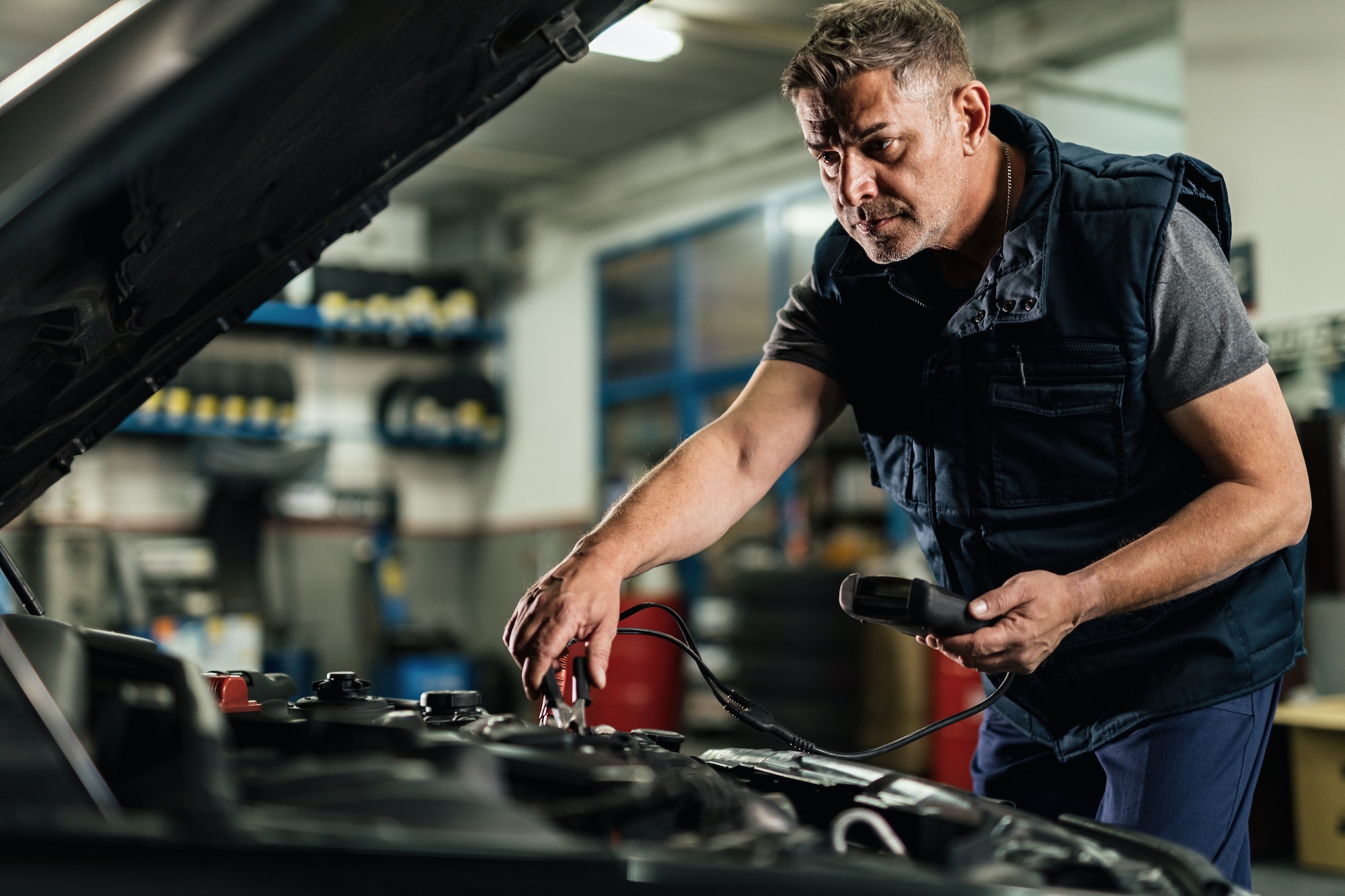 Auto mechanic repairing an engine and doing car battery check at workshop.